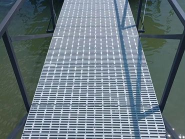 Metal walkway with railings over water casting shadows.