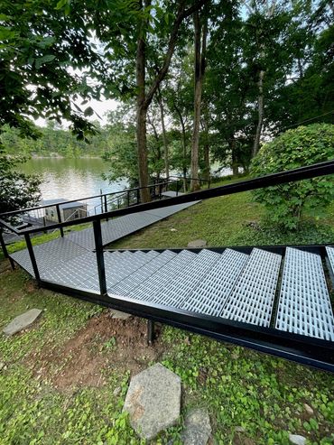 Metal stairs lead down to a lakeside dock surrounded by trees.