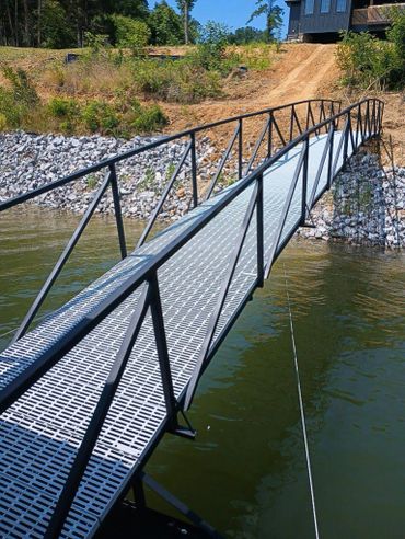 Metal pedestrian bridge over a lake leading to a dirt path.
