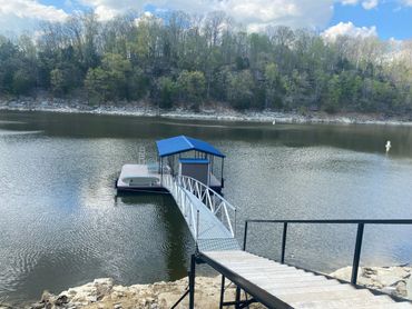 Dock extending into a calm lake with a blue-roofed shelter and forested shoreline.