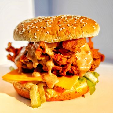 Close-up of a crispy fried chicken sandwich with cheese and sauce.