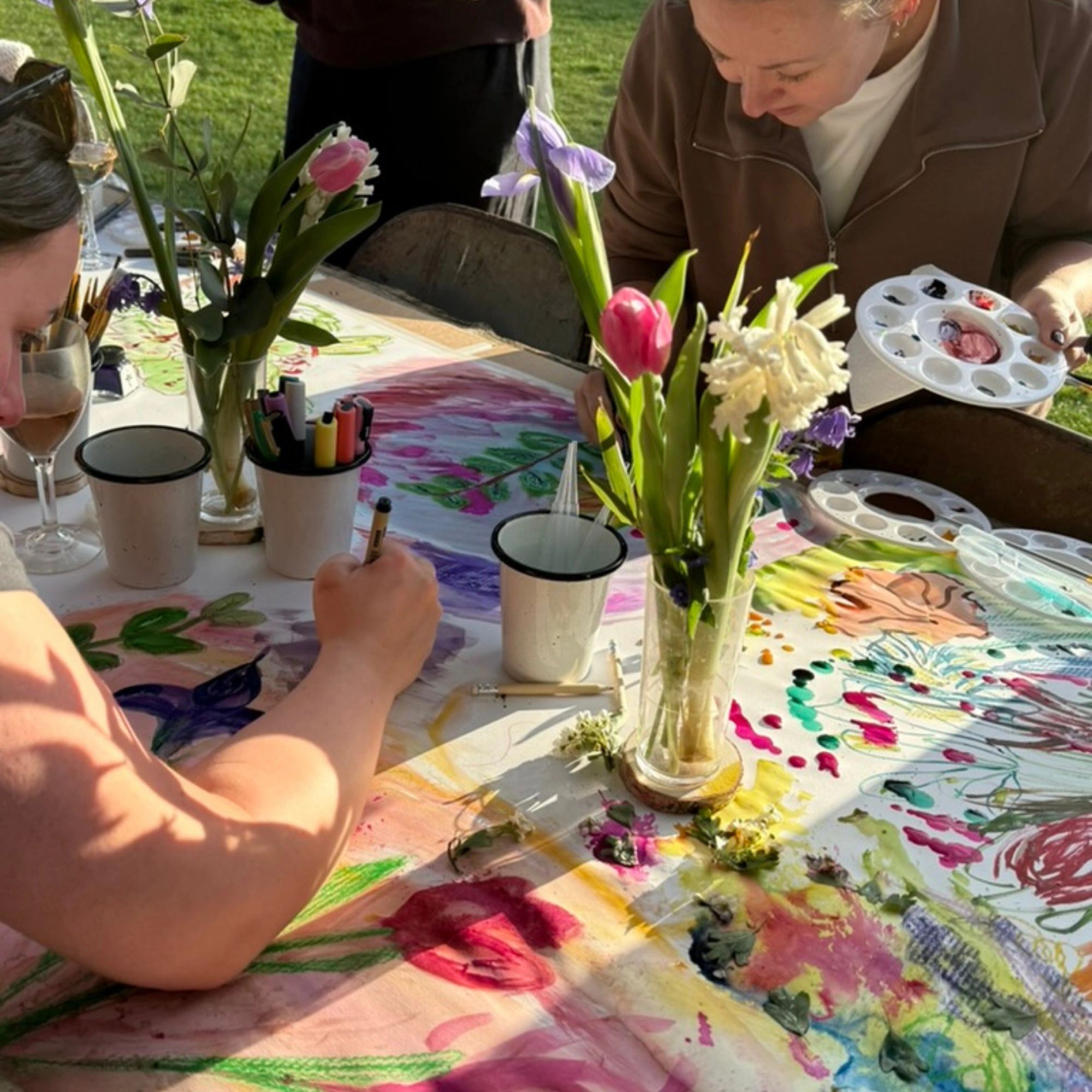 People painting colorful floral designs at a table outdoors.