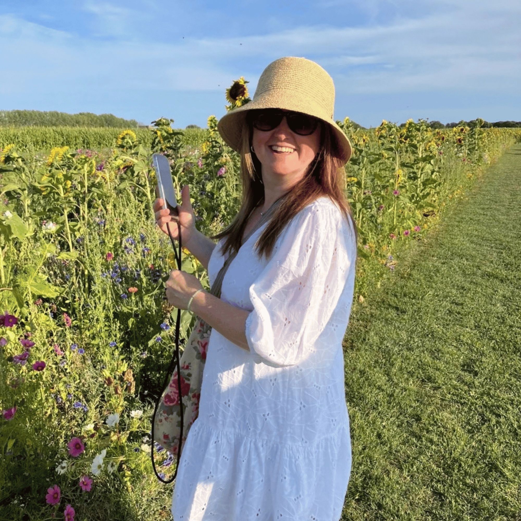Woman smiling in sunflower field wearing hat and sunglasses.