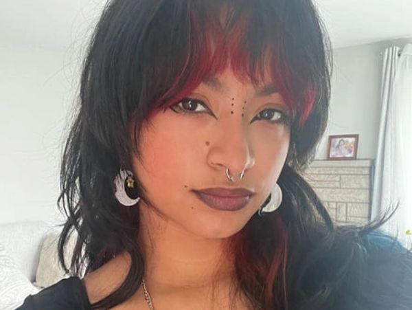 Young woman with black and red hair, wearing crescent moon earrings and a septum ring.