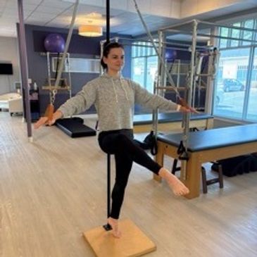 Woman balancing on a Pilates apparatus with outstretched arms.
