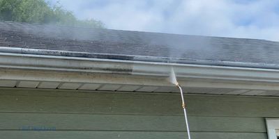 Picture of a pressure washer cleaning gutters on the side of a house.