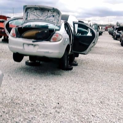 an old car parked in a scrap yard with doors and truck open