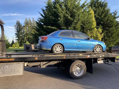 A blue junked car loaded on a roll back truck.