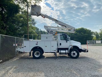 Bucket truck parked near a fence and tall trees