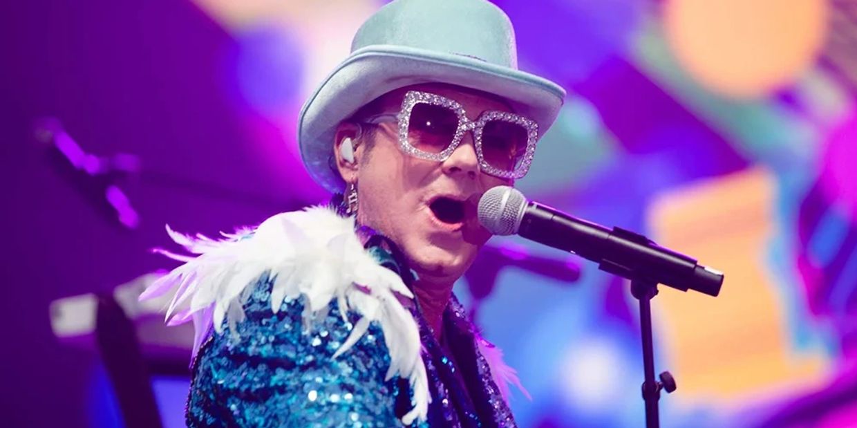 Performer in a sparkling blue outfit singing on stage with a microphone.