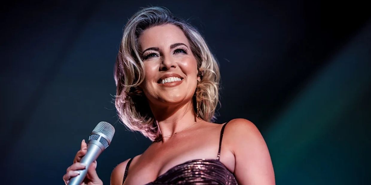 A joyful woman singing on stage with a microphone.