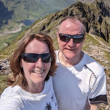 A smiling couple wearing sunglasses on a mountain peak.