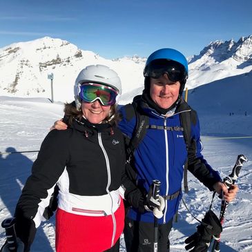Two skiers smiling with snowy mountains in the background.