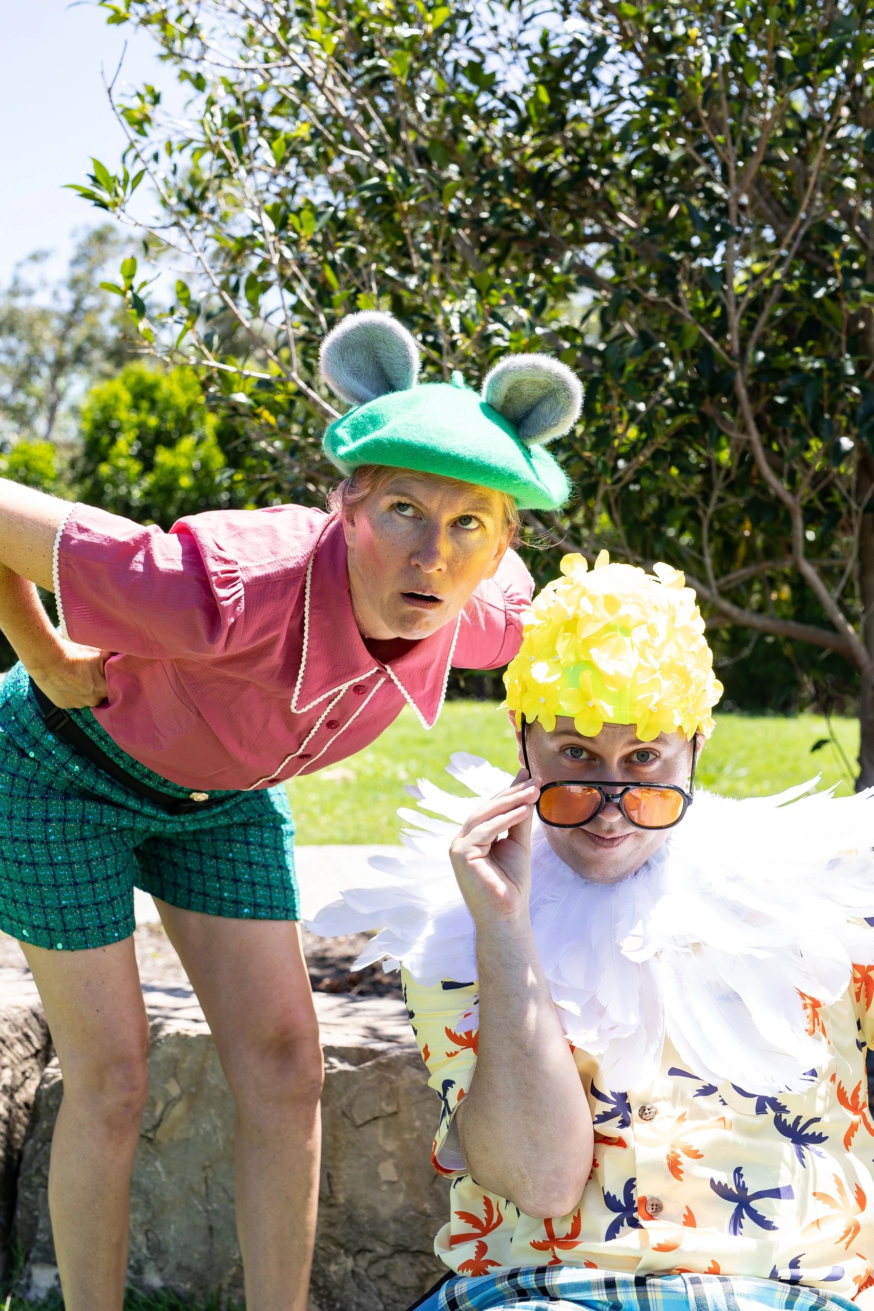 Two people in whimsical costumes posing outdoors with greenery in the background.