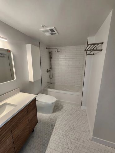 Modern bathroom with white tiles, wooden vanity, and a bathtub with shower.