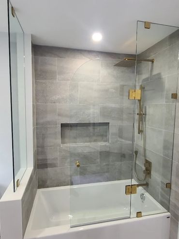 Modern bathroom with a bathtub and glass shower enclosure with gold fixtures.