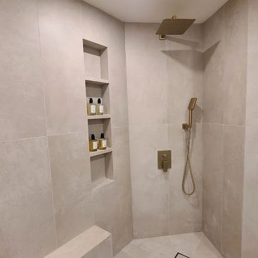 Modern beige tiled shower with built-in shelves and gold fixtures.