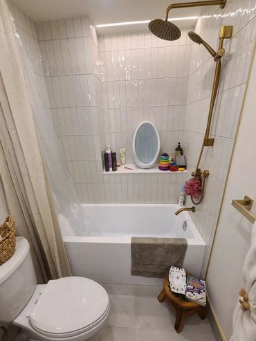 Modern bathroom with white tiles, gold fixtures, and kid-friendly bath toys.