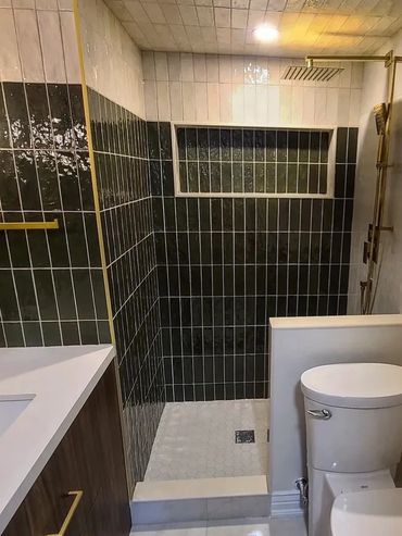 Modern bathroom with dark tiled shower and gold fixtures.