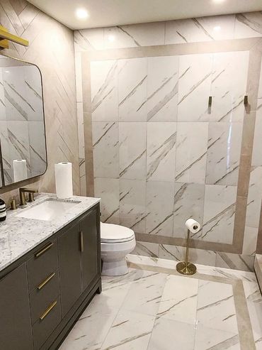Modern bathroom with marble tiles, gray vanity, and gold accents.