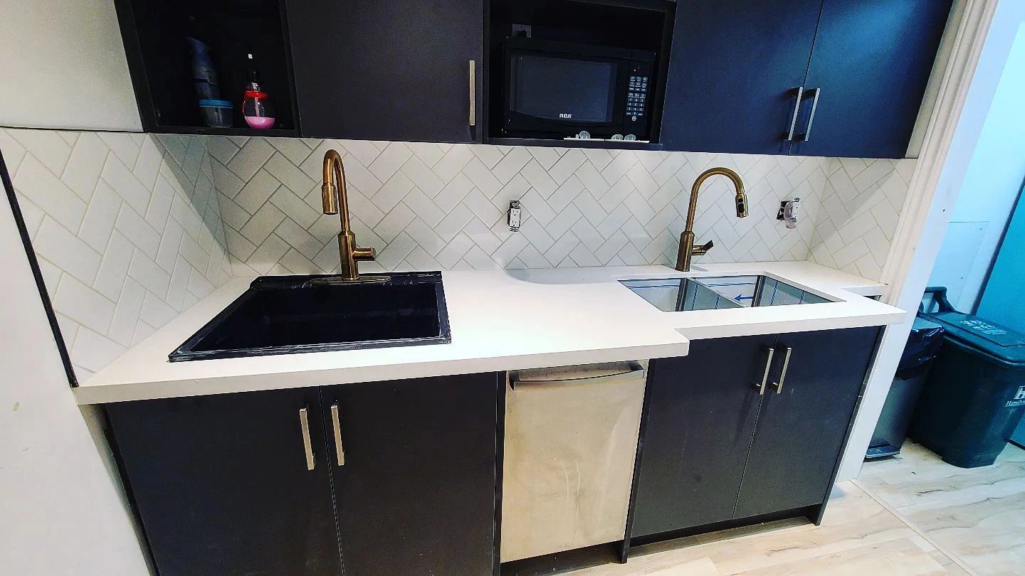 Modern kitchen with dual sinks, brass faucets, and dark cabinetry.