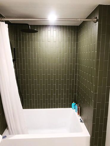 Modern bathroom with olive green tiles and a white bathtub.