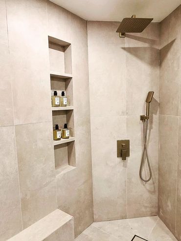 Modern beige tiled shower with built-in shelves and brass fixtures.
