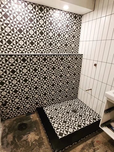 Black and white geometric tiled bathroom with a small sink and unfinished floor.