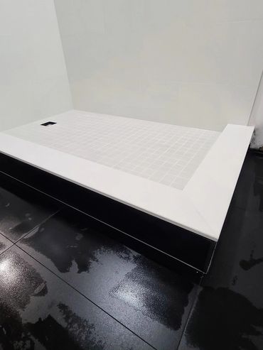 Modern minimalist shower base with white tiles and black glossy floor.