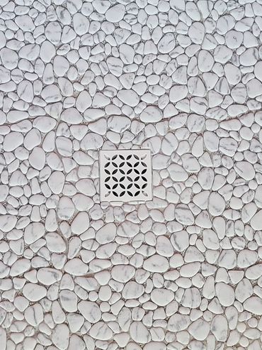 A central drain surrounded by white pebble tiles on the floor.