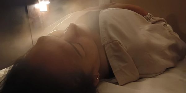 Person lying down in a softly lit room with mist or smoke around.