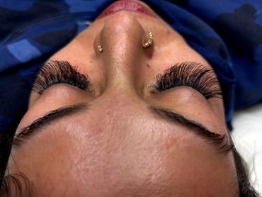Close-up of a person with thick eyelash extensions and gold nose rings.