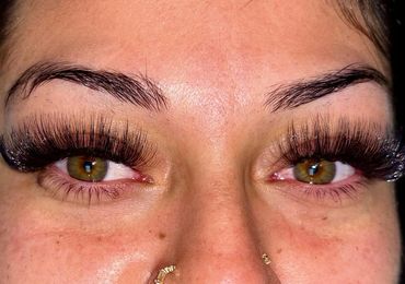 Close-up of eyes with thick, voluminous false eyelashes and gold nose rings.