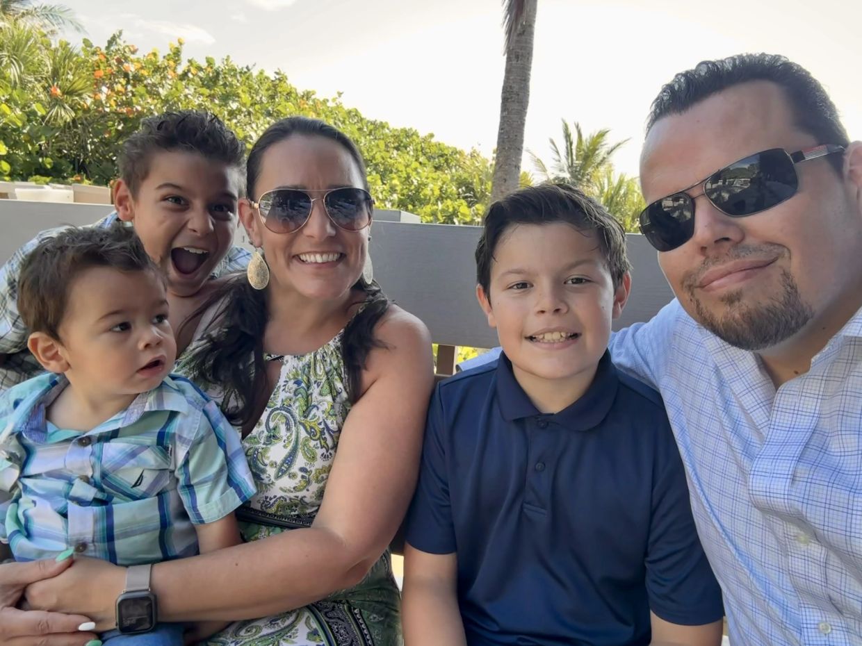 A happy family of five posing together outdoors on a sunny day.