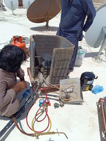 Technician repairing an air conditioning unit outdoors with tools and equipment scattered around.فني صيانة مكيفات بالرياض يقوم بإصلاح وحدات التكييف الخارجية وتعبئة الفريون.