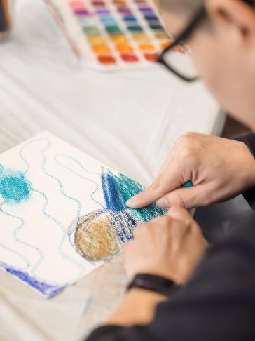 Person finger painting with crayons and watercolors.