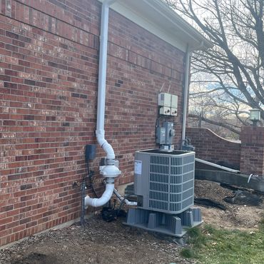 Exterior radon mitigation system with fan and vent pipe installed alongside a home's AC unit for rad