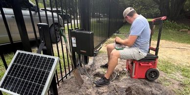 Man installing solar-powered gate system outdoors.