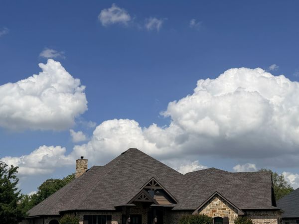 A house with a dark roof under a blue sky with fluffy white clouds.