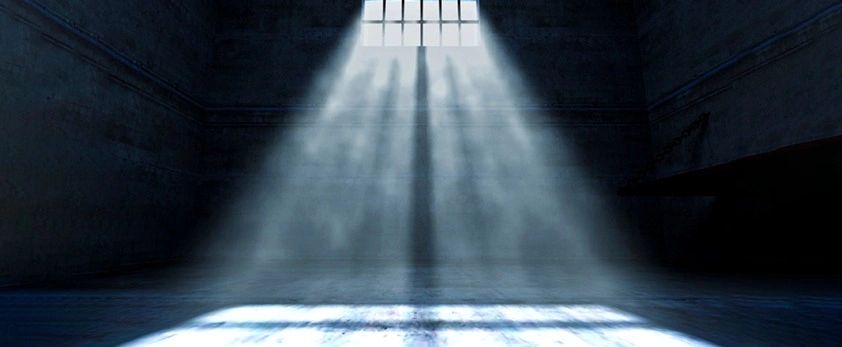 Sunlight beams through a barred window into a dark, empty room.