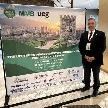 Man in formal attire standing next to a conference banner at the 18th European Digestive Surgery course.