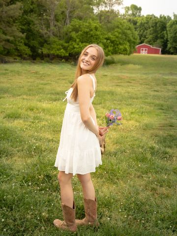 Young woman in white dress and boots holding flowers in a green field.