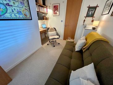 Counselling room showing a large sofa, chair and desk area. soft lighting, and warm and inviting fee