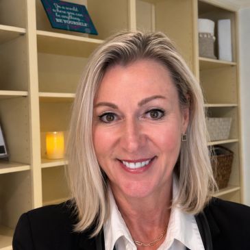 Professional woman with blonde hair smiling in an office setting.