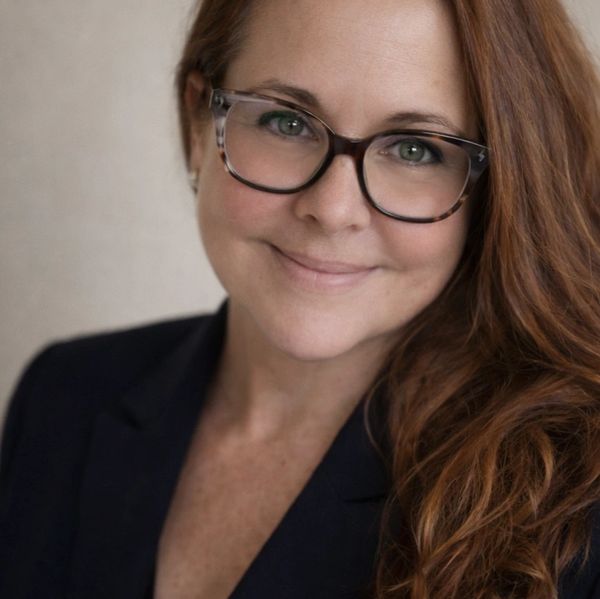 Smiling woman with glasses and long red hair in a dark blazer.