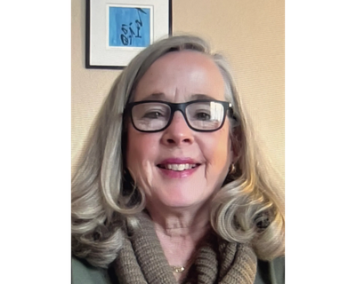 Smiling woman with glasses and wavy blonde hair.