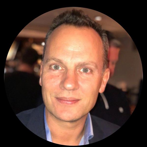 Close-up portrait of a smiling man in a suit jacket and blue shirt.