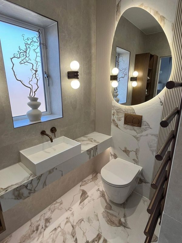 Marble bathroom with wall-hung basin and toilet, round mirror and heated towel rail