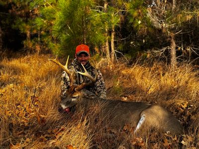 Hunter posing with a large buck in a forest clearing.