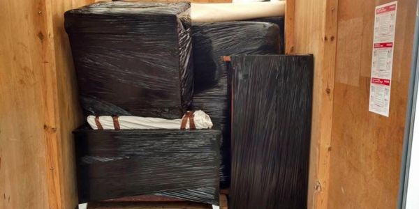 Furniture pieces wrapped in black plastic inside a wooden crate.